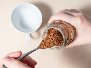 female hand spooning up instant coffee from jar