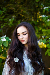 a teenager girl with dark long wavy hair in white dress standing in the apple garden