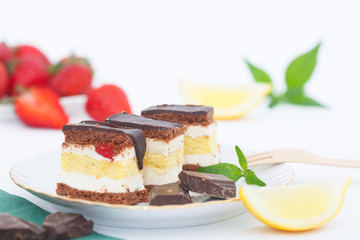 Lemon cake with chocolate glaze. Strawberries and mint leaves in background.