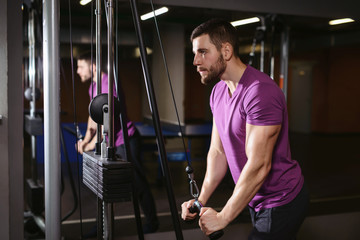 Young adult bodybuilder healthy fitness man doing triceps overhead extension rope exercise. Workout in public gym and sporty lifestyle concept