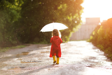 Happy child  with an umbrella playing out in the rain in the summer outdoors - obrazy, fototapety, plakaty