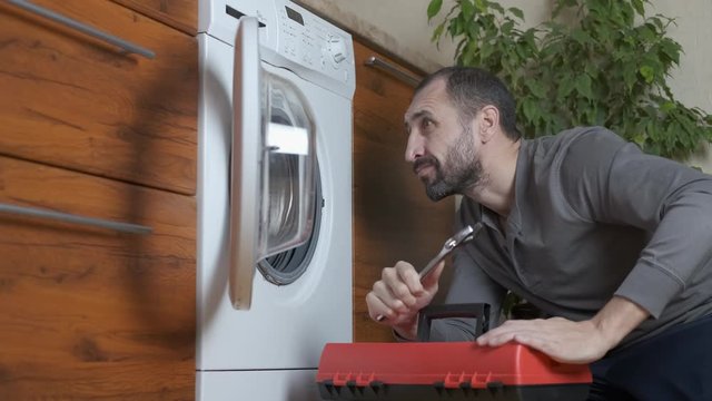 Washing machine repair. A man with tools looks into a broken washing machine.