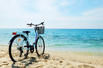 Fototapeta premium Feminine bicycle of comfort class with empty basket on the sandy beach of mediterranean sea. Blue cruiser bike on sunny day at sea shore with a lot of copy space for text.