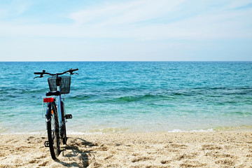 Fototapeta premium Feminine bicycle of comfort class with empty basket on the sandy beach of mediterranean sea. Blue cruiser bike on sunny day at sea shore with a lot of copy space for text.