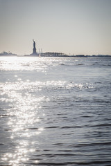 Statue of Liberty shape against light from lower tip of Manhattan - New York City, NY