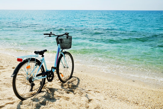 Feminine bicycle of comfort class with empty basket on the sandy beach of mediterranean sea. Blue cruiser bike on sunny day at sea shore with a lot of copy space for text.