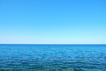 Fototapeta na wymiar Beautiful seascape on sunny day with wind patterns on calm azure water and clear blue sky without clouds. Ocean view with horizon, background with a lot of copy space for text.