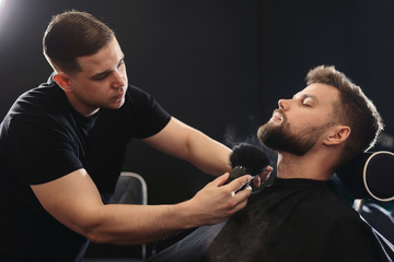 Getting perfect shape. Close-up side view of young bearded man getting beard haircut by hairdresser or barber at barbershop