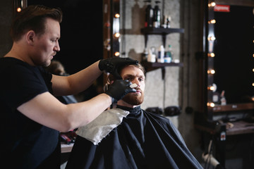 Closeup of barber shaving man beard with straight steel razor blade at barbershop. Brutal hairdresser at work