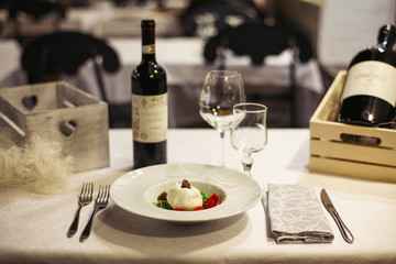 Light wooden table setting: white plates, rustic dark table cloth with mozzarella, cheese, vine