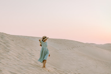 Young woman walking on the sand dunes in the desert during the sunset