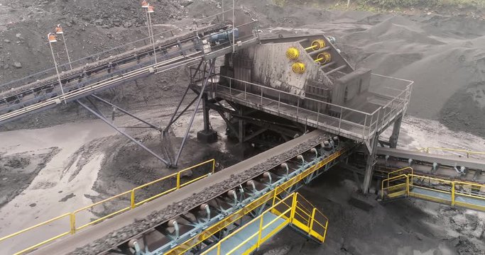 From above Open pit mine, breed sorting, mining coal, extractive industry. Top view coal falling from the moving belt conveyor into pile at coal mine with coal miners working on the background.