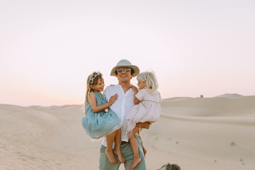 Happy father holding two daughter in the desert in Dubai