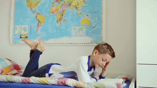 Engaged teenage boy reading book in bed at home
