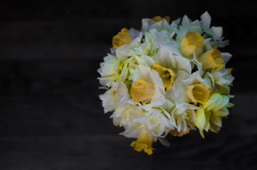 A bouquet of flowers on a dark wooden background. White narcissus in a vase. Place for your text. Top view.