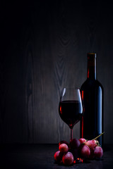 Red wine in glass and bottle and bunch of grapes on wooden table