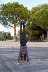 Obraz premium Young handsome flexible male in sportswear with roller skates doing handstand on road in beautiful city park