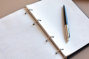 Open notebook with pen lying on it on beige desktop. Notepad sheets on silver brackets, automatic ballpoint pen in silver-black color. Concept business, work at home. Copy space. Top view, close-up.