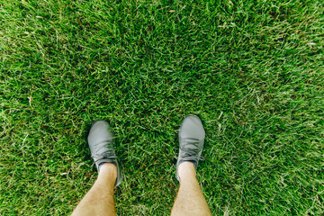Male feet in running shoes standing on the grass, above view