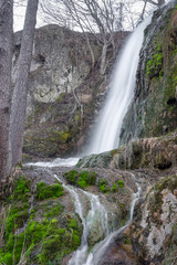 Obraz premium Close up, long exposure view of a sunlit waterfall with soft streams of water falling down red rocks covered by green moss