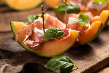 Sliced melon with ham and basil leaves, served on a wood chopping board