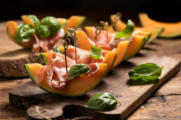 Sliced melon with ham and basil leaves, served on a wood chopping board