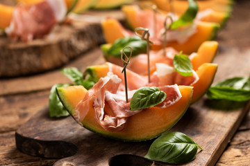 Sliced melon with ham and basil leaves, served on a wood chopping board