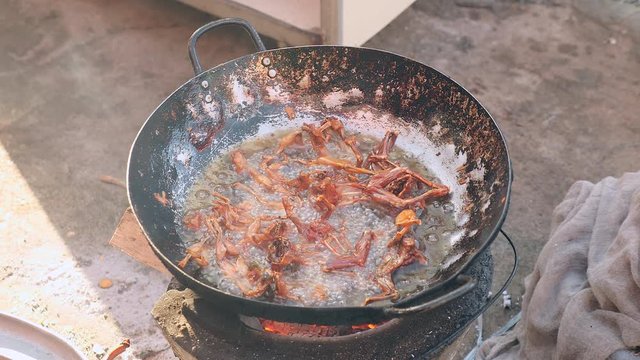 Woman using metal tongs to stir deep-frying frogs in a wok over a household stove ( close up )