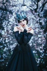 grim lady with pale white skin and dark hair beside flowering tree, witch turns with black crow...