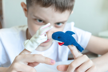 A caucasian boy playing different roles by using finger puppets, toys for expressing his emotions, agression, fear and freandship as a part of psychotherapy