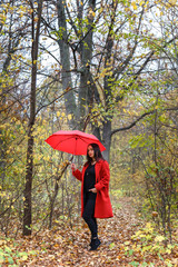 Woman dressed in a red coat walk in autumn park with a red umbrella.
