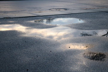 Early sunlight in reflection of water puddle on pavement street 