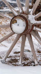 Fototapeta premium Vertical Close up of the wooden wheel of an old wagon against a snowy terrain in winter