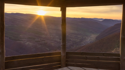 Framed view through the wooden summer house on a valley of village Dojkinci and beautiful sunrise in the mountains