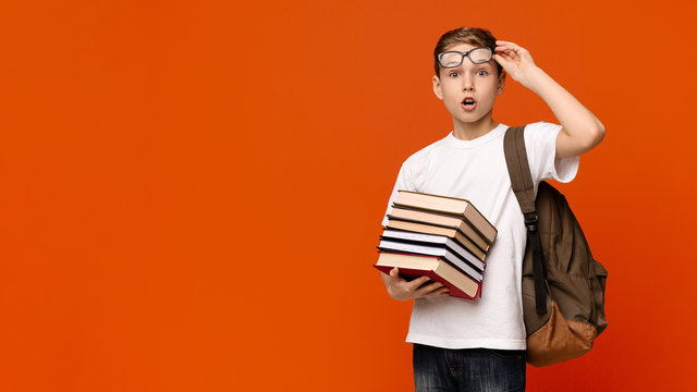 Shocked schoolboy in glasses holding stack of books