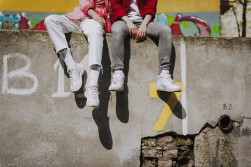 Two stylish girls sitting together on parapet