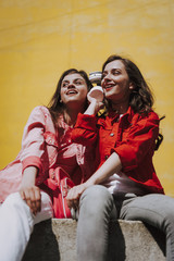 Two hipster girls listen to music on parapet