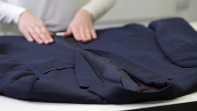Close-up of female employee careful hands inspecting suit jacket from inside out in process of work in dry cleaning salon. Woman worker checking client's blazer before taking in dry clean