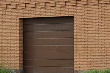 facade of a brown garage with a closed gate on a brick wall outside in green grass
