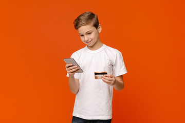 Smiling teenage boy holding credit card and smartphone