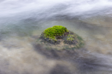 Long exposure, minimalist, simple composition of a rock covered by vivid green moss in the middle of the river