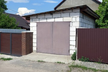 Fototapeta na wymiar white brick garage with brown gates and metal fence on the street by the road