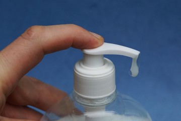 finger presses white dispenser in a plastic bottle with liquid soap