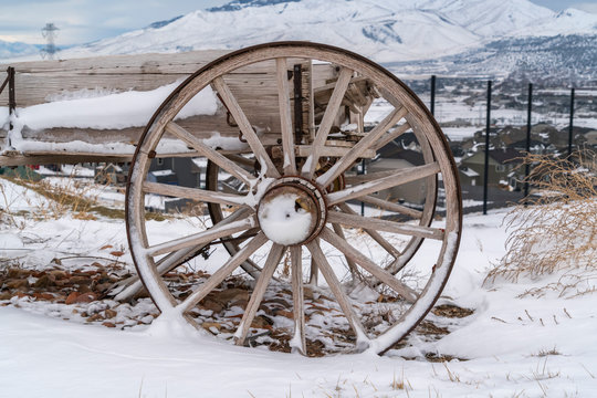 Rusty wheel of a wooden cart against a rocky ground covered with snow in winter