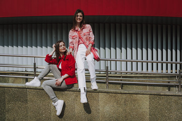 Two hipster girls sitting on city ramp parapet