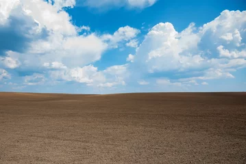 Schilderijen op glas Empty brown soil of field and blue sky for natural background © Yakov