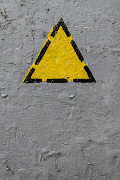 Yellow triangle on a old gray coarse metaic painted surface