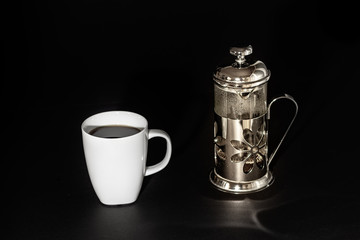 A cup - mug of coffee with a plunger - french press coffee maker over black background.