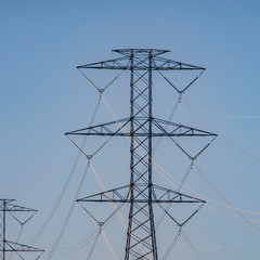Clear Square Row of tall utility towers against pale blue sky with puffy clouds