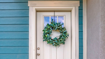 Panorama Facade of a home with a simple leafy wreath hanging on the white front door © Jason